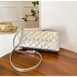 Detail of silver quilted crossbody bag with metal logo on a wooden cafe table