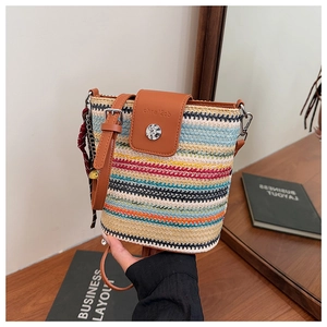 Détail d'un sac seau en paille arc-en-ciel avec rabat et bandoulière en cuir brun