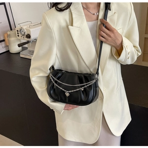 Détail du sac nuage noir plissé avec chaîne à cœur sur fond de blazer beige