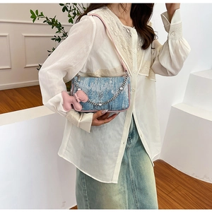 Detail of light blue denim shoulder bag with pink strap and cute puppy pendant