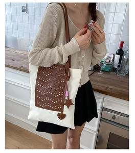 Detail of contrast canvas tote bag with brown faux leather pocket and heart pendant