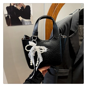 Close-up of black pebbled leather bucket bag with pearl bow charm and N D 2 lettering