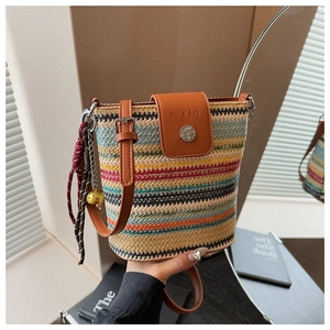 Détail du sac seau en paille rayé avec rabat en cuir marron et pompon décoratif