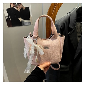 Detail of pink faux crocodile bucket bag with decorative white lace bow and pearl charm