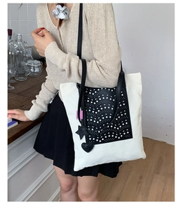 Detail shot of large canvas tote bag with black contrast leather panel and charm accents