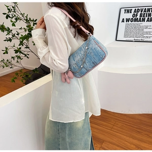 Detail of light blue denim shoulder bag with pink trim and silver chain strap