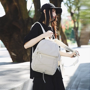 Minimalist beige outdoor backpack with elastic cord design worn by a female model outdoors