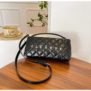 Detailed view of black quilted leather crossbody bag with silver letter charms on a table