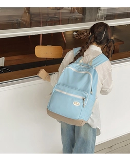 Outdoor shot of a light blue and khaki minimalist backpack worn by a person in a white shirt