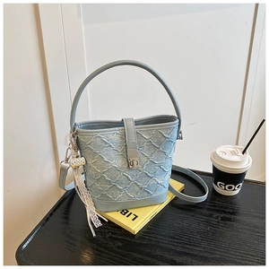 Dettaglio borsa a secchiello in denim azzurro con trapuntatura e nappa in pizzo chic