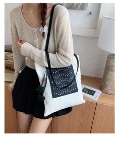Detail of canvas tote bag with contrast leather cutout and decorative charms on model