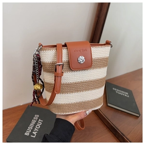 Gros plan d'un sac seau tissé avec rayures, rabat en cuir et breloque clochette dorée