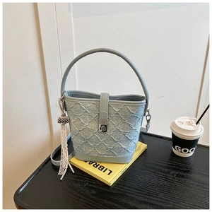 Dettaglio della borsa a secchiello in denim azzurro con texture a griglia e nappa in pizzo