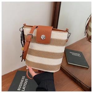Détail du sac seau tressé avec garniture en cuir marron et breloque décorative en foulard