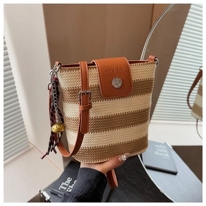 Détail du sac seau en paille tressée avec rabat en cuir, texte embossé et boucle argentée