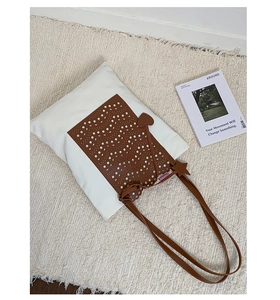 Detail of laser-cut brown patterned overlay on a white canvas tote bag with heart charms