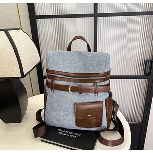 Detail of blue denim backpack with brown leather trim and metallic buckle accents