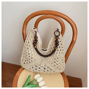 Detail of woven straw tote bag featuring intricate hollow patterns and dark wood bead handles
