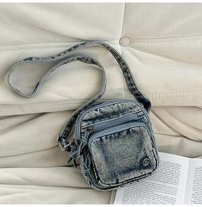 Détail du sac bandoulière en jean délavé avec fermetures éclair et logo métallique M