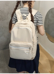 Rear view of model wearing cream nylon backpack with layered storage and logo