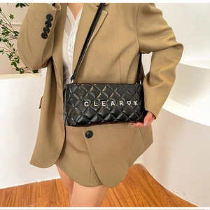 Detail of a black quilted crossbody bag with silver metal logo worn with a beige suit