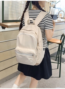 Detail view of a beige minimalist nylon backpack with multiple zippered front pockets