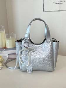 Silver metallic bucket bag with lace bow and pearl charms on a minimalist background