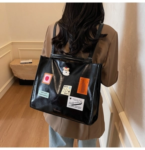 Detail of black glossy tote bag with stylish patches worn as a backpack in a cozy room