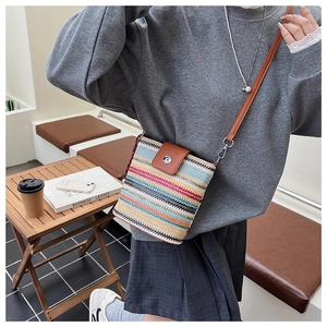 Détail d'un sac seau rayé en paille avec rabat en cuir marron et boucle métallique