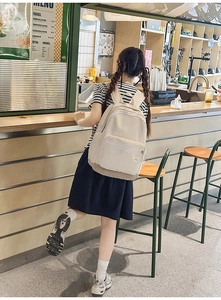 Detailed back view of a beige minimalist backpack worn in a modern cafe setting