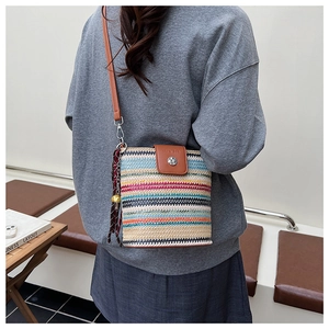 Gros plan du sac seau en paille rayé avec bandoulière en cuir et détail de pompon