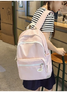 Detail of light pink nylon backpack featuring multi-layered zippers and brand logo