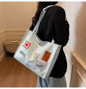 Close-up of a mint blue glossy tote bag with Shiba Inu and apple patches on a model