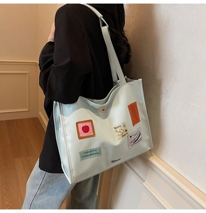 Detail of light mint green tote bag featuring artistic patches and polished leather finish