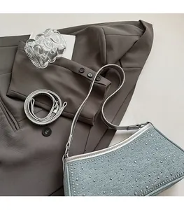 Dettaglio della borsa in denim con borchie argentate su sfondo blazer grigio scuro