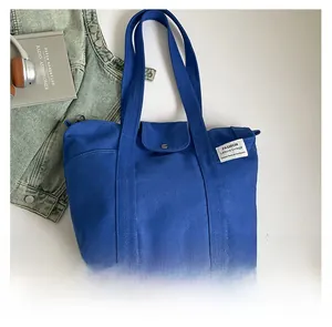Detail of blue canvas tote bag featuring metal clasp closure and woven logo label