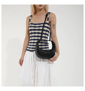 Detail of small crescent bag in black grained leather with metal handle and shoulder strap