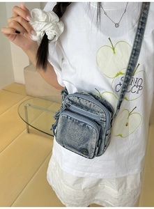 Détail du sac à bandoulière en denim bleu clair avec fermetures éclair et logo en métal