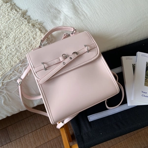 Pink faux leather backpack on a soft bed, featuring a top handle and buckle details