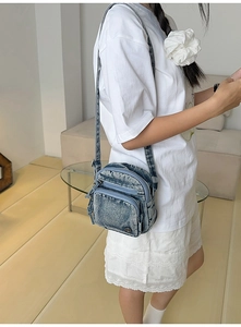 Vue de côté d'un sac bandoulière en denim délavé montrant la structure des poches multicouches