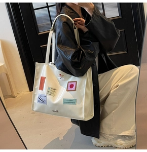 Close-up of white leather tote bag with colorful cartoon embroidery and brand logo details