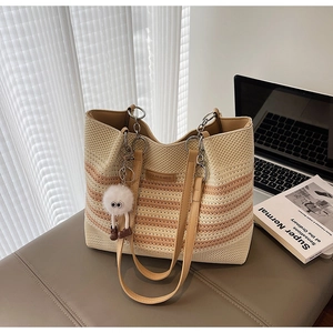 Détail d'un grand sac cabas tissé à rayures marron avec doubles anses en cuir sur un tabouret