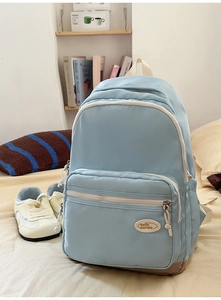 Close-up of light blue casual backpack with multiple zipper pockets on a bed