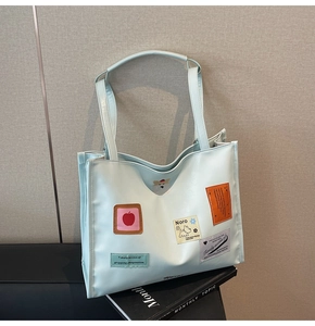 Detail of light blue faux leather tote bag with cartoon patches and graphic embroidery