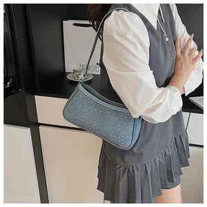 Dettaglio della borsa a spalla in denim blu con borchie argentate e chiusura a zip