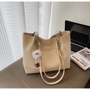Détail du sac cabas tissé beige montrant le logo en cuir et la bandoulière chaîne