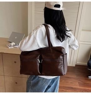 Detail view of large dark brown leather travel tote bag with dual front zipper pockets