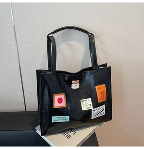 Detail of black leather tote bag featuring cute cartoon patches and embroidery designs