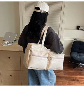Detail of a large cream tote bag with dual front zipper pockets shown in use