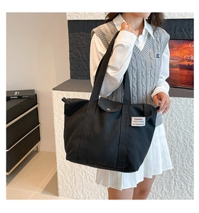 Detail of black canvas tote bag showing reinforced stitching and white brand label